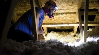 Person adding insulation in attic of house