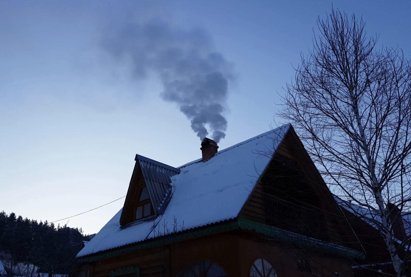 House in winter with snow on the roof and smoke coming from its chimney